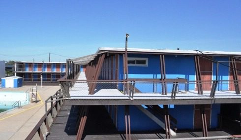 Blue building with outdoor walkway and pool.