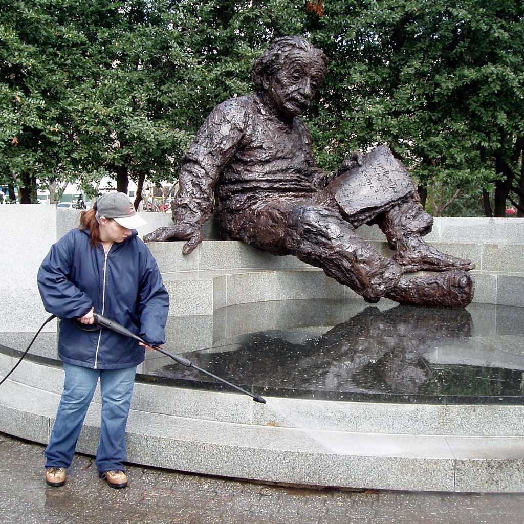 Person standing beside a large seated bronze statue near a water fountain outdoors.