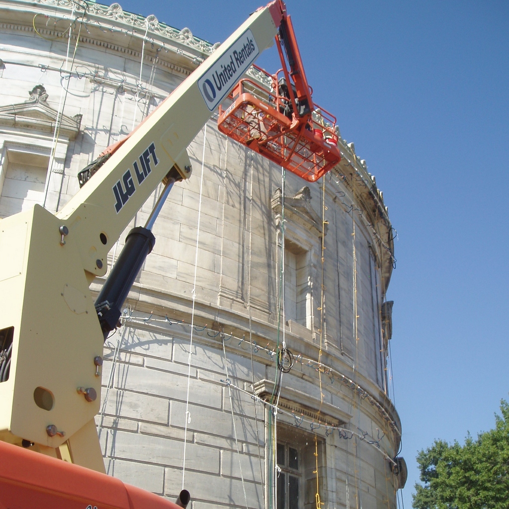 Crane lifting equipment near a classical building under clear blue sky.